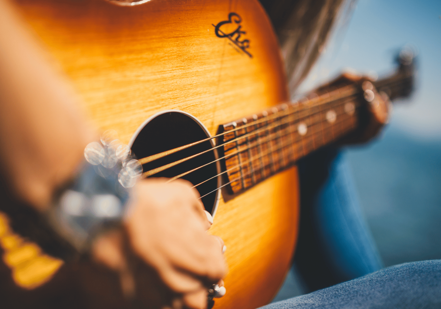 Close-up of an acoustic guitar being played, with the player’s hand strumming the strings on a sunlit wooden body.